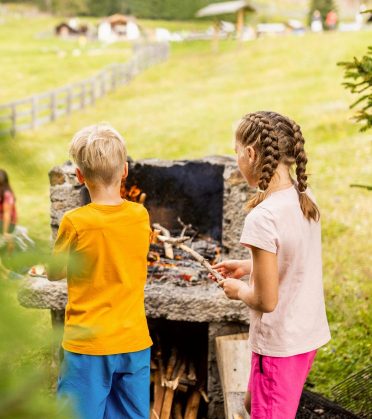 Two children barbecue at a stone fire pit on the meadow.