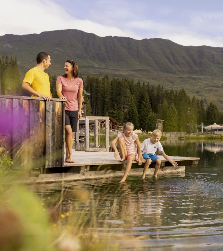 A family on a wooden jetty by the lake, the children dangling their feet in the water.
