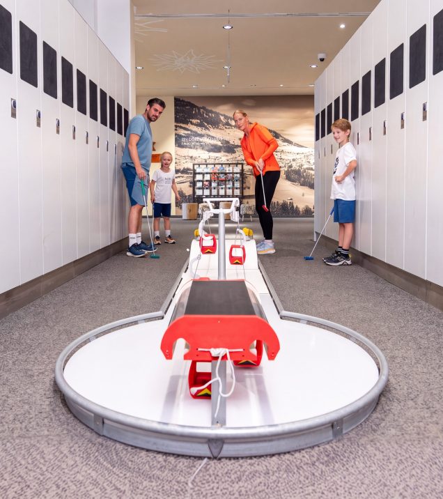 A family playing indoor mini golf in the Indoor Arena Fiss, in the foreground a course with red gondolas as an obstacle.