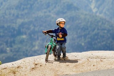 Ein kleiner Junge mit Helm schiebt sein Kinderrad über eine Kuppe im Bikepark.
