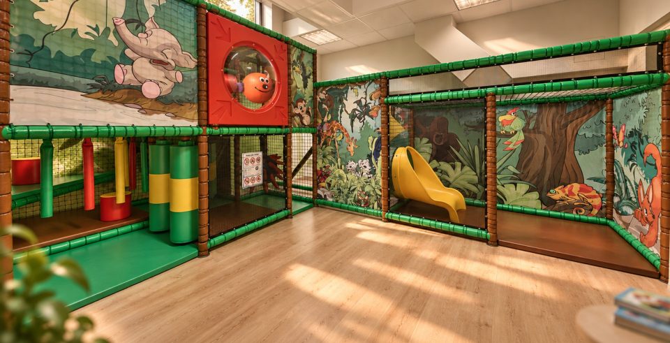 Softplay-Anlage im Dschungel-Look in Sonnis Kids Club: Klettergerüst mit grünen Stangen, gelbe Rutsche und bemalte Wände mit Elefant und Bäumen.