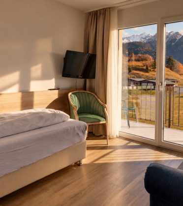Room in the staff house with a bed, a blue sofa and an open balcony door, the mountains outside.