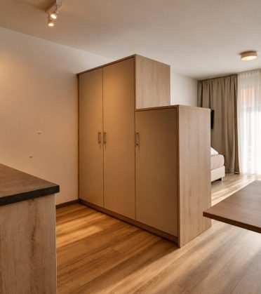 Room in the staff house with a kitchenette, wardrobe, dining table and large window.
