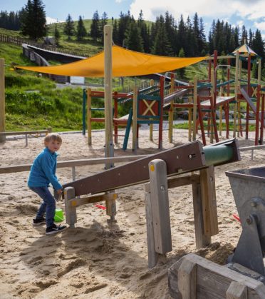 A boy playing at a water channel in the sand, a climbing frame with a sun sail behind him.