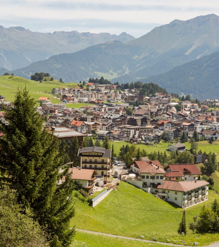 View over the village with hotels and houses, the mountain range behind.