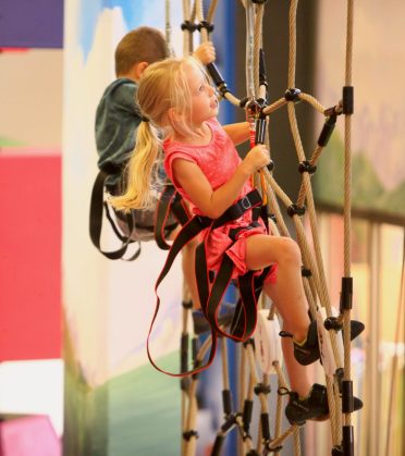 Two children on safety lines climbing through a rope course.
