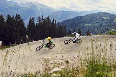 Zwei Kinder fahren auf Mountainbikes durch eine Steilkurve auf dem Pumptrack.