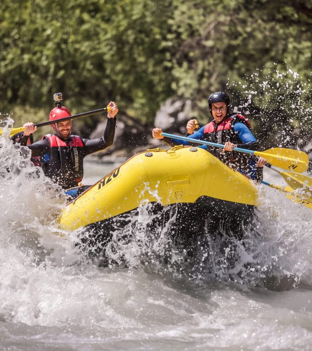 Two paddlers cheer in a yellow H2O Adventure raft as it runs through white, foaming whitewater.