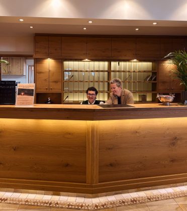 The illuminated wooden reception desk at Hotel DreiSonnen, two staff members behind it.