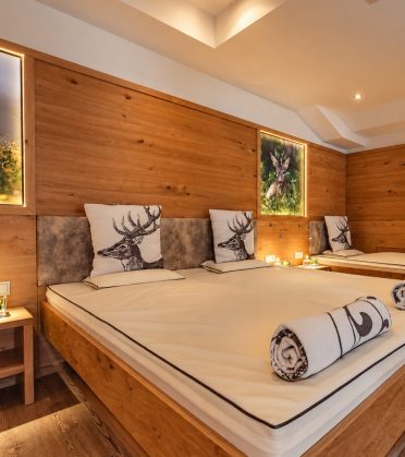 Ruheraum im Hotel DreiSonnen mit breiter Liege, Hirschkissen und gerollten Decken, an der Holzwand ein beleuchtetes Bild mit einem Reh.