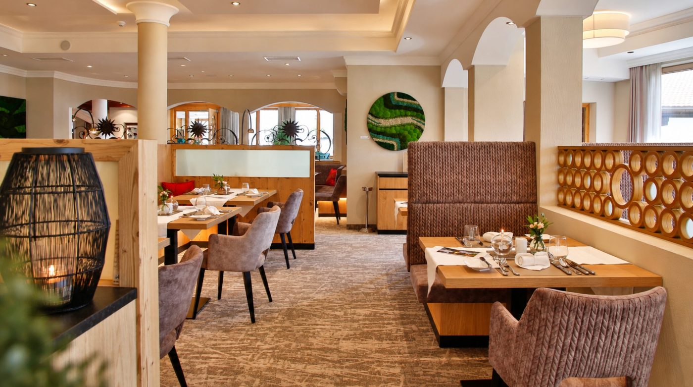 Speisesaal im Hotel DreiSonnen mit gedeckten Tischen, Sitznischen mit gepolsterten Bänken und Sesseln, an der Wand ein rundes Moosbild.