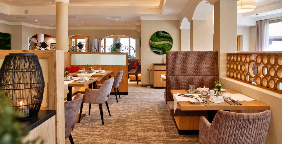 Speisesaal im Hotel DreiSonnen mit gedeckten Tischen, Sitznischen mit gepolsterten Bänken und Sesseln, an der Wand ein rundes Moosbild.