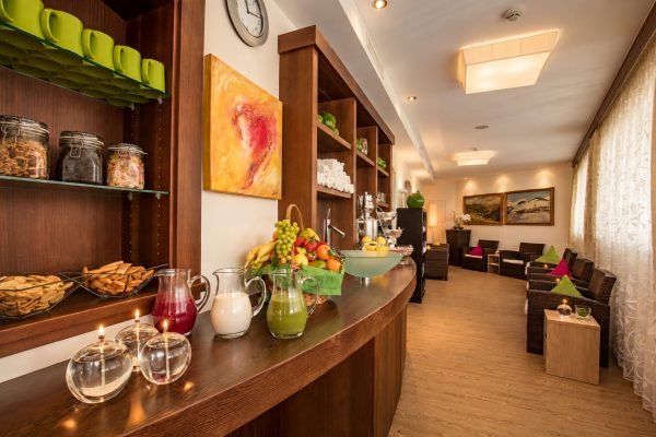 Theke der Teestube im Hotel DreiSonnen mit Obstkorb, Säften in Glaskrügen und Windlichtern, dahinter die Lounge mit Sesseln.