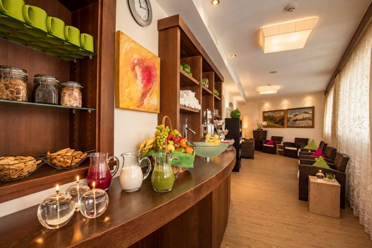 Counter of the tea room at Hotel DreiSonnen with a fruit basket, juices in glass jugs and lanterns, behind it the lounge with armchairs.