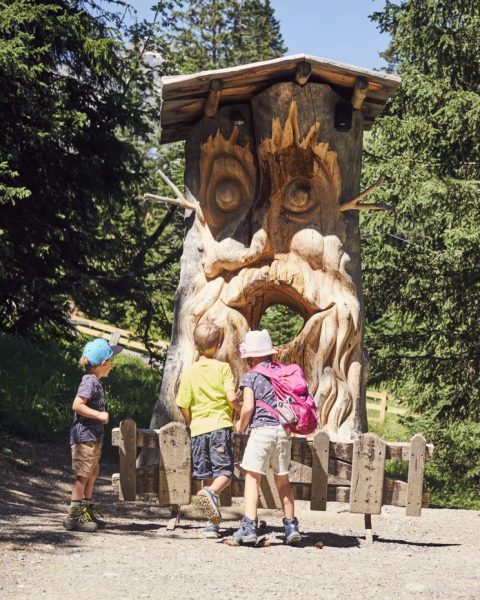 Children playing on a carved wooden figure at the edge of a themed trail.