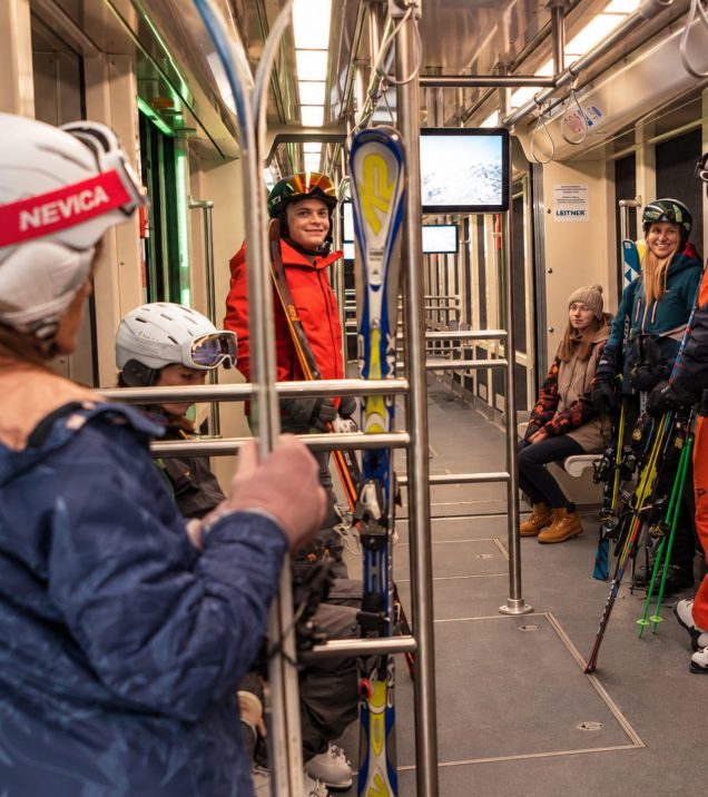 Winter guests with skis and helmets in a carriage of the Serfaus U-Bahn, on their way to the ski area.