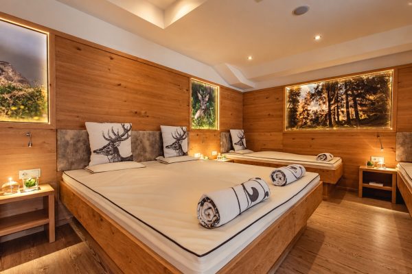 Ruheraum mit Holzwänden und breiten Liegen, auf den Kissen Hirschmotive, an den Wänden beleuchtete Waldbilder und kleine Kerzen.
