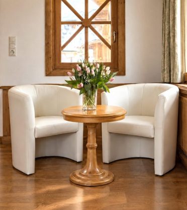 Two white armchairs at a round wooden table with tulips, behind them a wooden window, in a room at Hotel DreiSonnen.