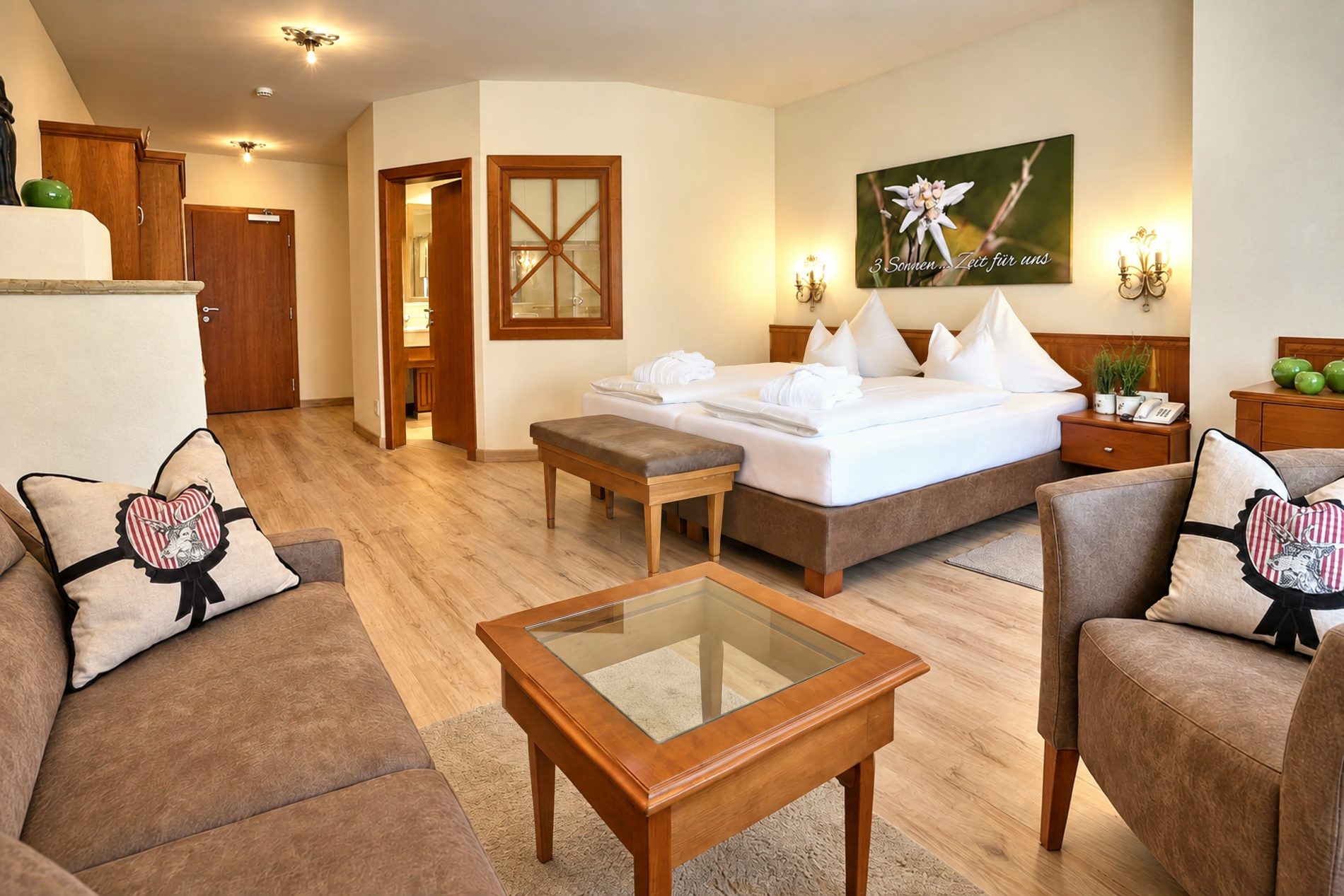 Seating group with coffee table in front of the double bed with an edelweiss picture in the Valentina room at Hotel DreiSonnen in Serfaus